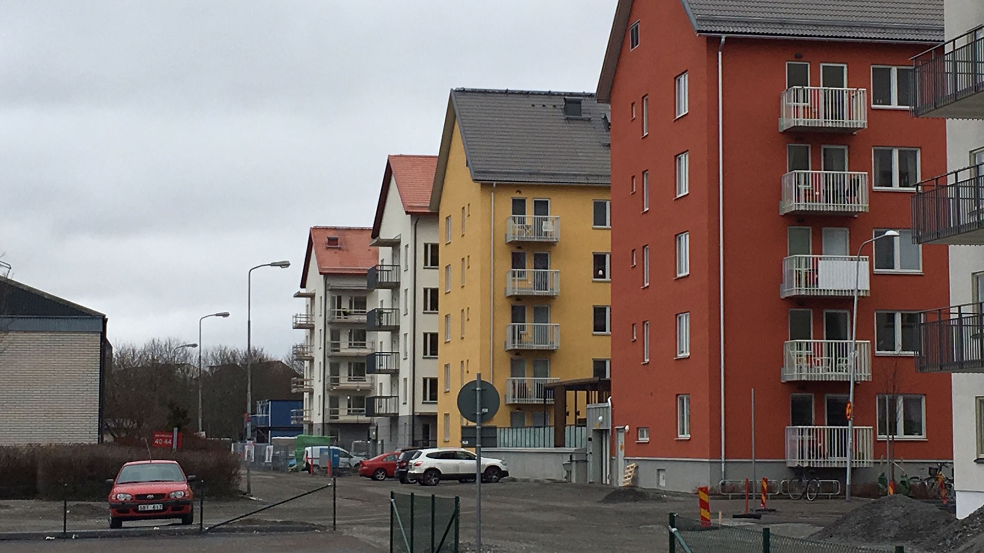 Kvarteret Falkarna är samverkan mellan Riksbyggen och Skanska. Bostadsområde med färgglada lägenhetsbyggnader och parkerade bilar på en molnig dag.