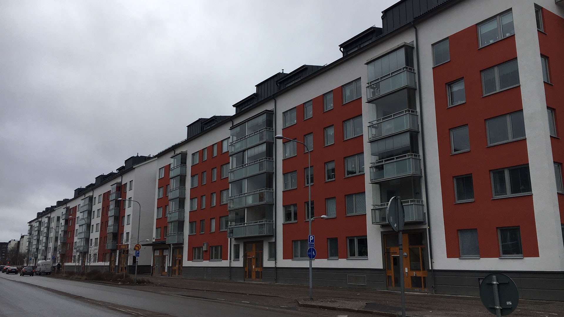 Torn-, Jakt- och Pilgrimsfalken är likadana. Moderna flerbostadshus med röda och vita fasader kantar en gata under en molnig himmel.