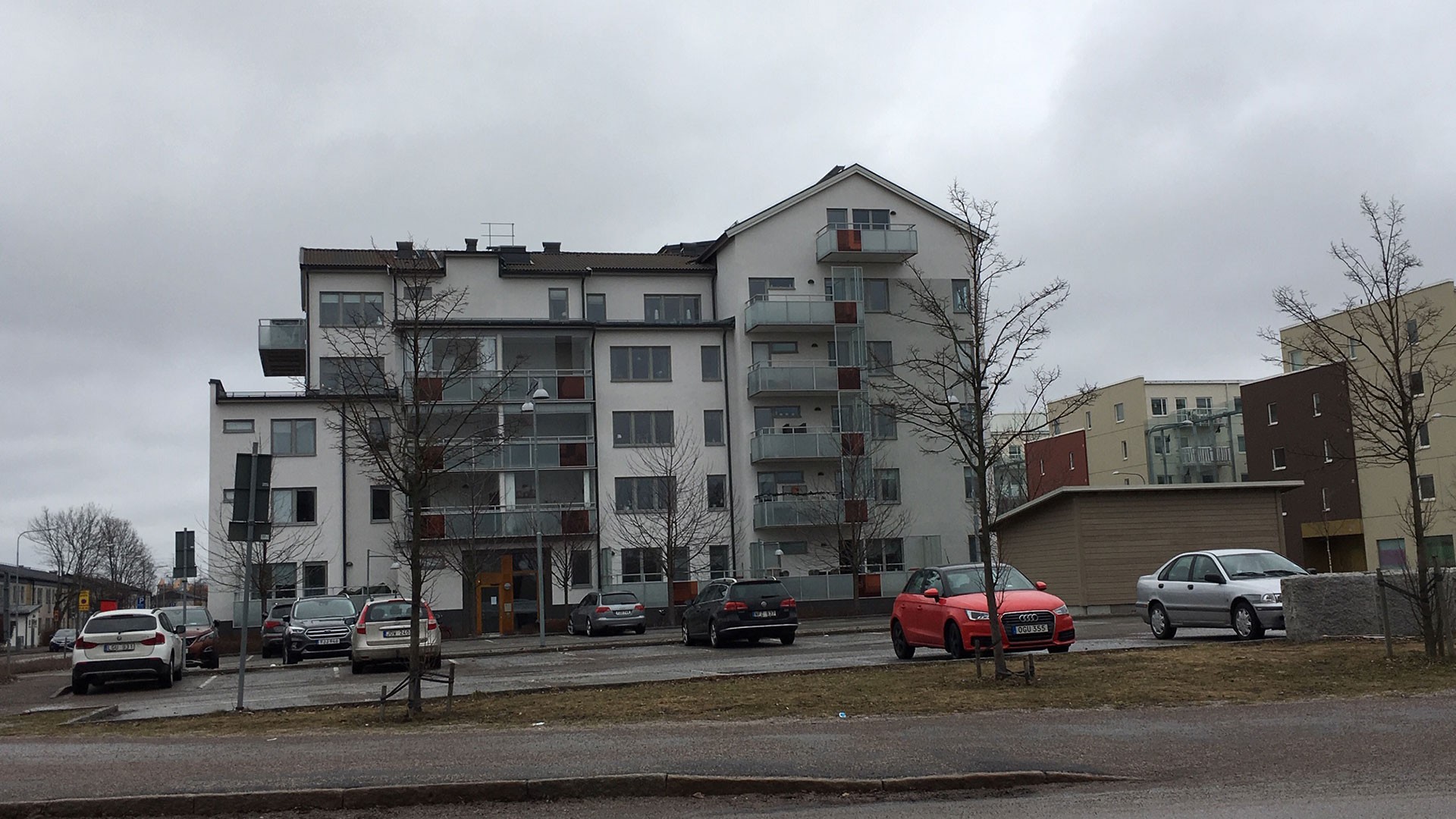 Vi har byggt fem etapper med flerbostadshus på uppdrag av Riksbyggen. Modern lägenhetsbyggnad med balkonger, parkerade bilar och molniga himlar.