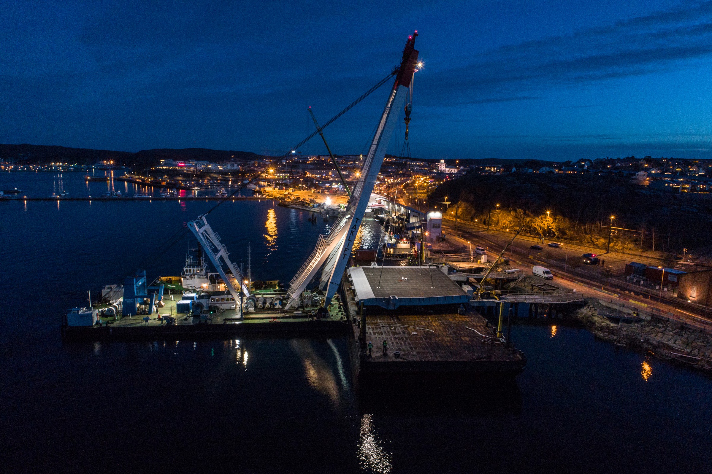 Rampen är 27 meter bred. Nattlig vy över en livlig hamn med upplysta kranar och stadsljus som reflekteras på vattnet.