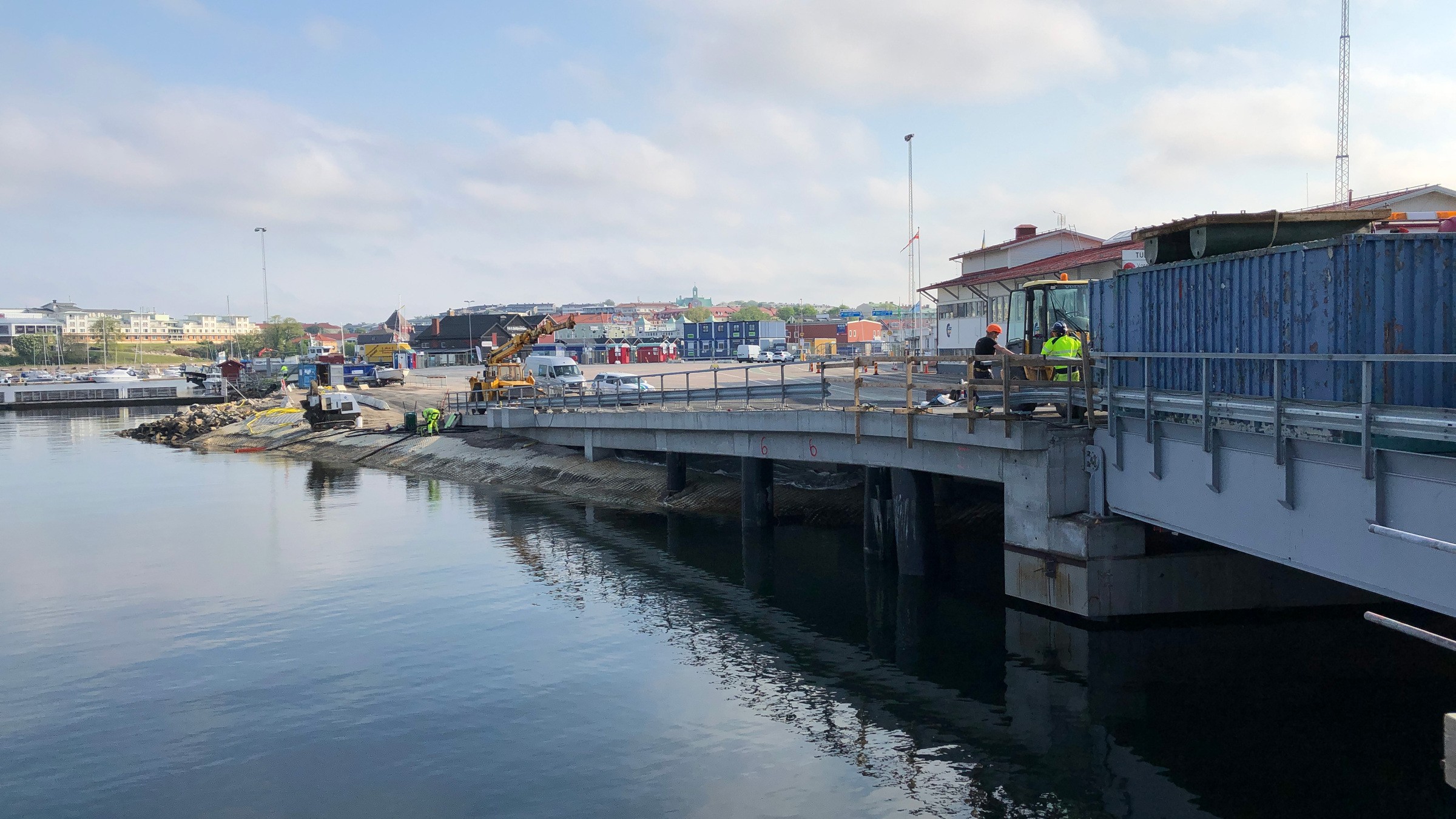 Vi ska renovera och bygga en 80 meter ny kaj. Byggarbetsplats vid vattenfronten med arbetare på en delvis byggd bro i ett hamnområde.