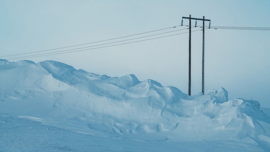 Snötäckt landskap med telefonstolpar och ledningar under en blekblå himmel.