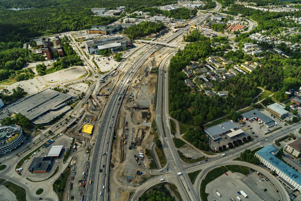 Flygvy av motorvägsbygge mitt i stadsmiljö med omgivande grönska.