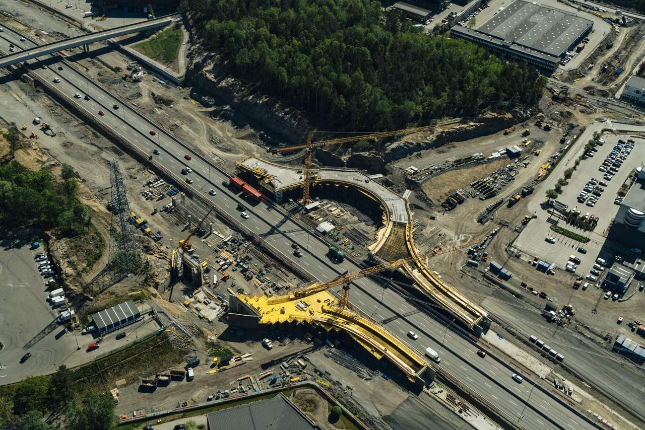 Flygvy över en stor motorvägsbyggarbetsplats med kranar och fordon i ett stadsområde.