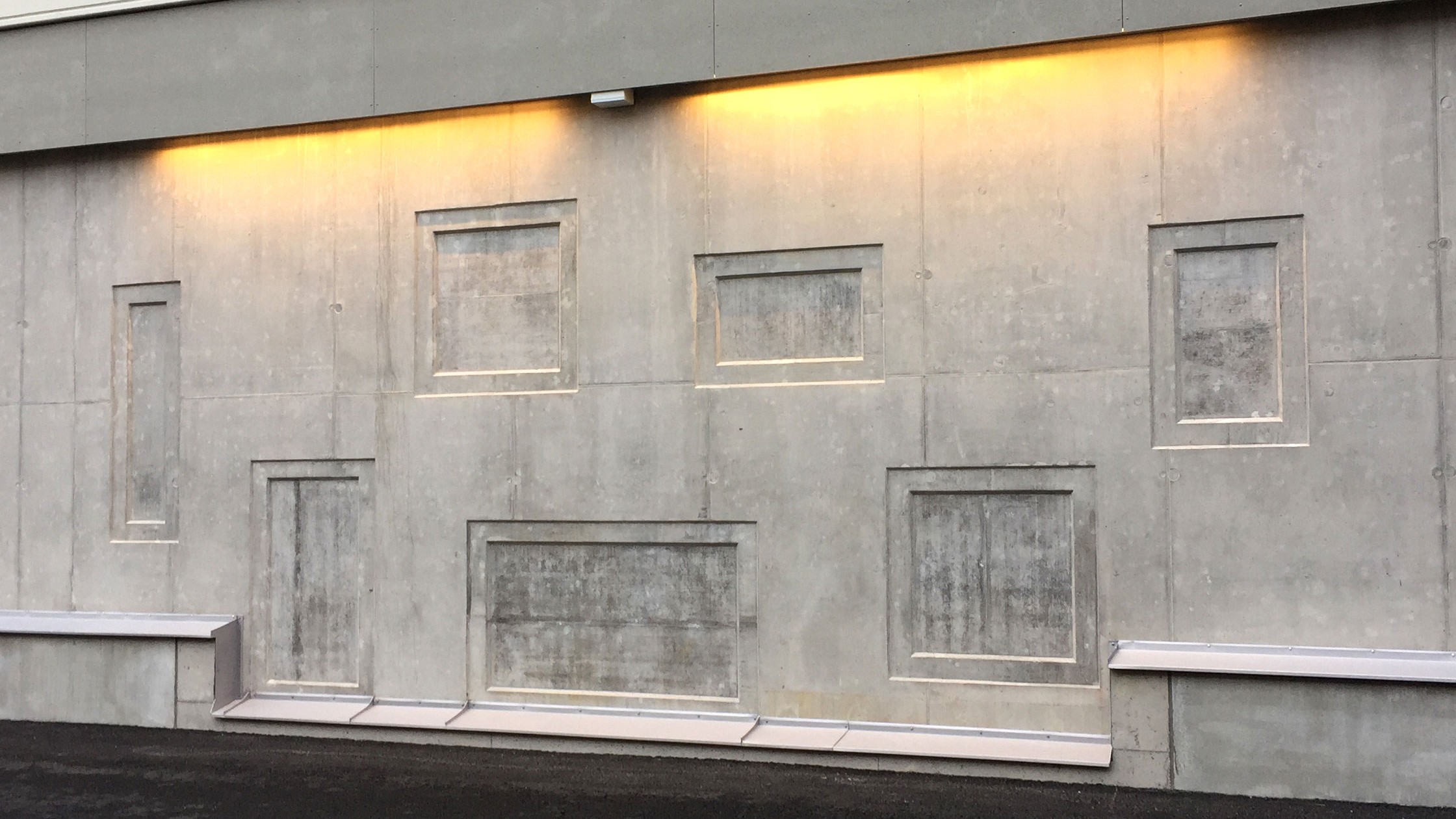 Betongen har formats och skapat en vacker utsmyckning. Betongvägg med indragna paneler och gul belysning, med minimalistisk arkitektonisk design.