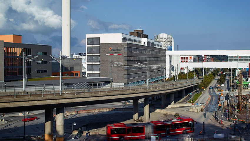 Bussdepån ligger mellan Hammarby Sjöstads huvudgata – Hammarby Allé och områdets kaj. Stadsmiljö med motorväg, moderna byggnader och stadstransporter i rörelse.