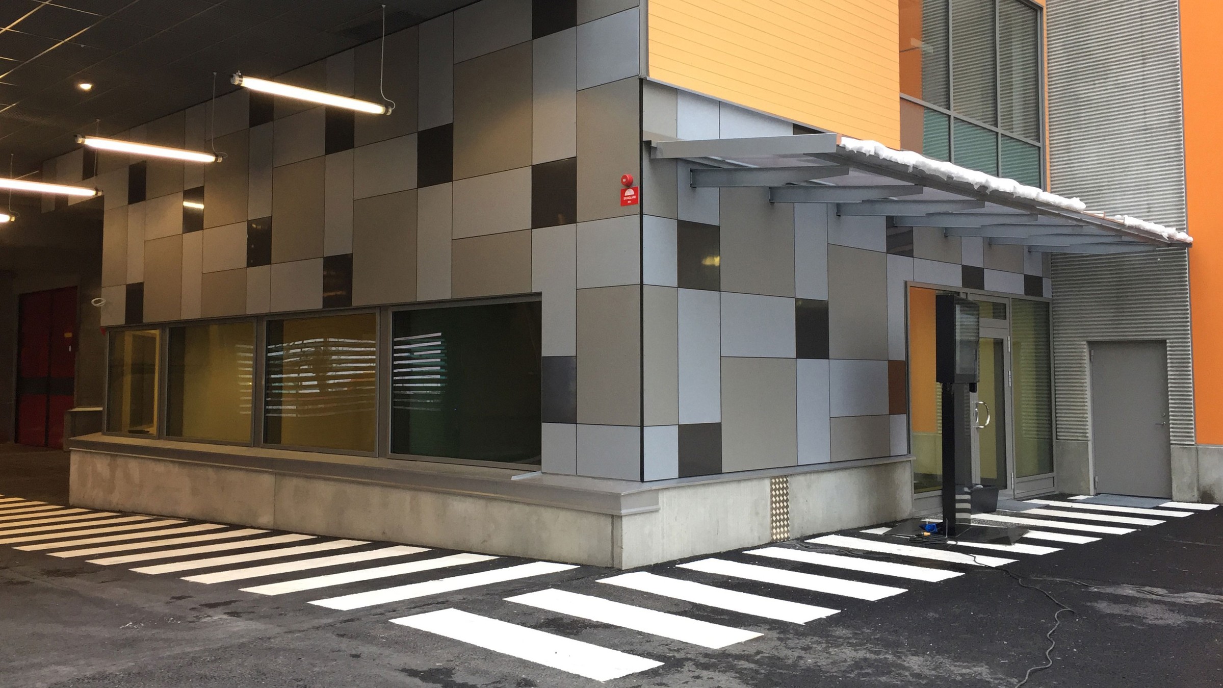 Då bussdepån ligger centralt så är det smidigt för bussarna att ta sig till och från depån. Modern byggnadsentré med geometriska paneler och övergångsställen på en belagd yta.