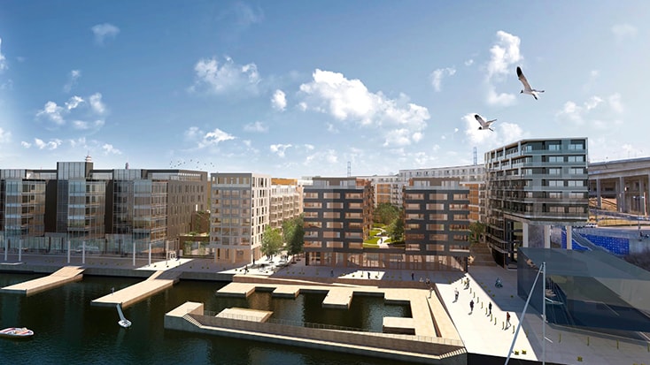 Fredriksdal bussdepå ligger i Hammarby Sjöstad, Stockholm. Modern stadsutveckling vid vattnet med byggnader för blandad användning och en livlig strandpromenad under en blå himmel.