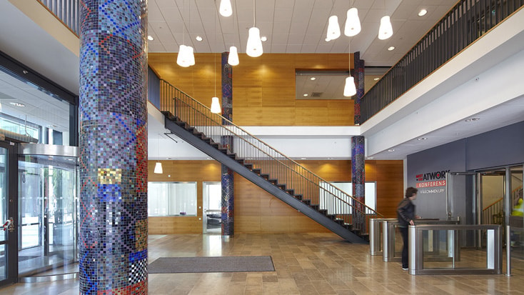 Modern kontorslobby med färgglada mosaikpelare, träväggar och en central trappa.