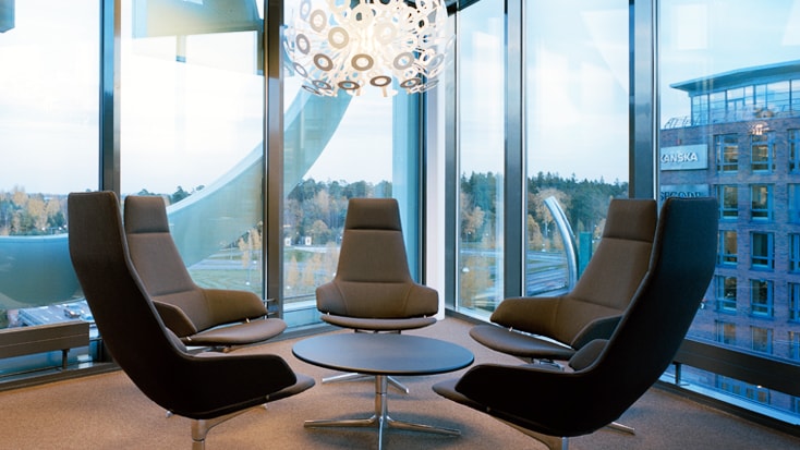 Modern office lounge with sleek chairs, round table, and large windows showcasing a cityscape.