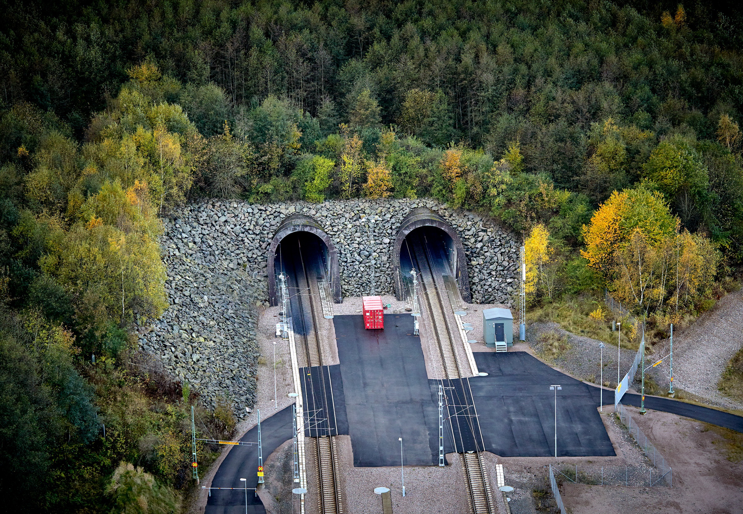 Hallandsås, flygfoto Två tågtunnlar kommer fram från en skogsklädd sluttning, med spår som leder till ett öppet område.