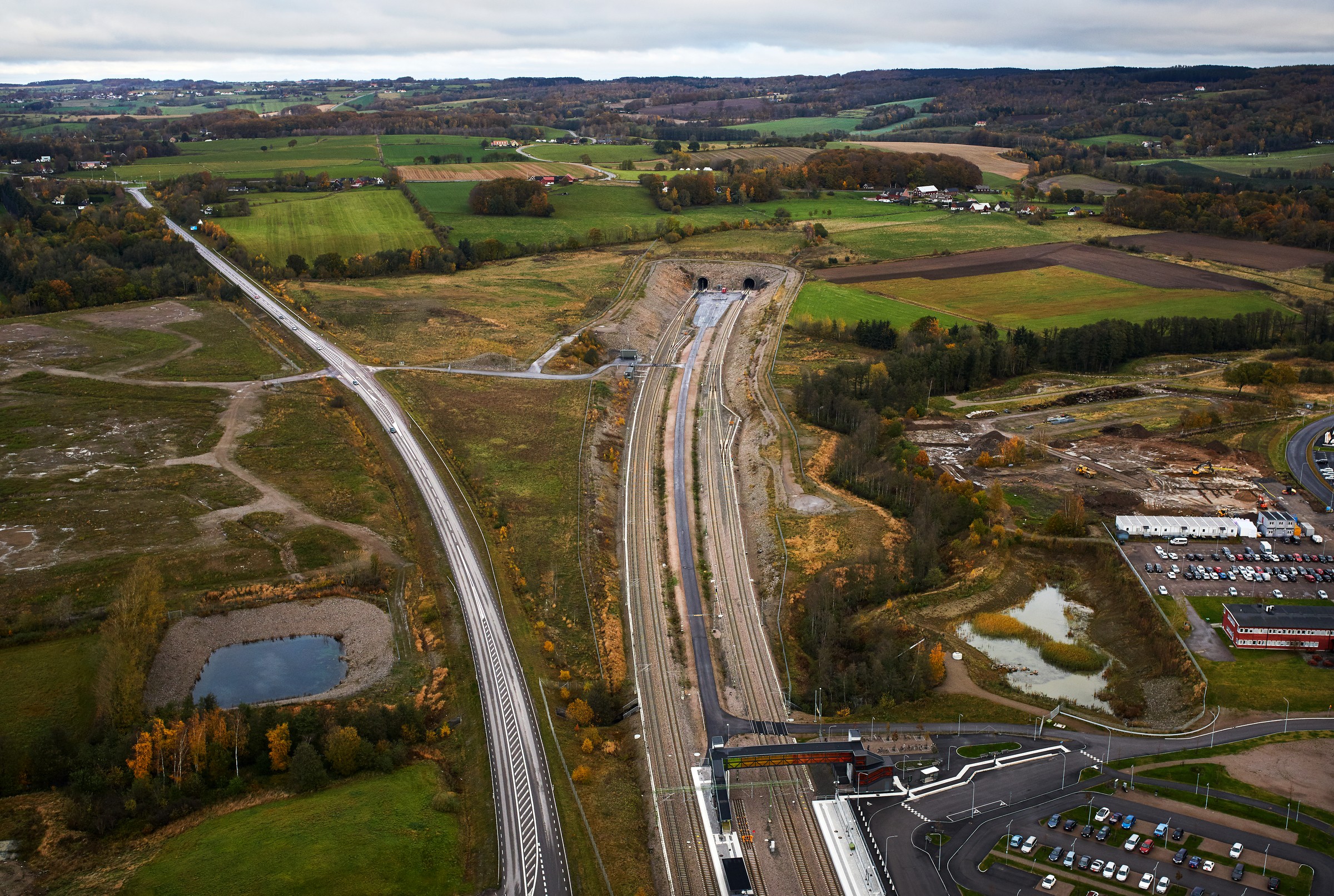 Hallandsås, flygfoto Flygvy över en järnvägsstation med spår, vägar och omgivande fält i ett lantligt landskap.
