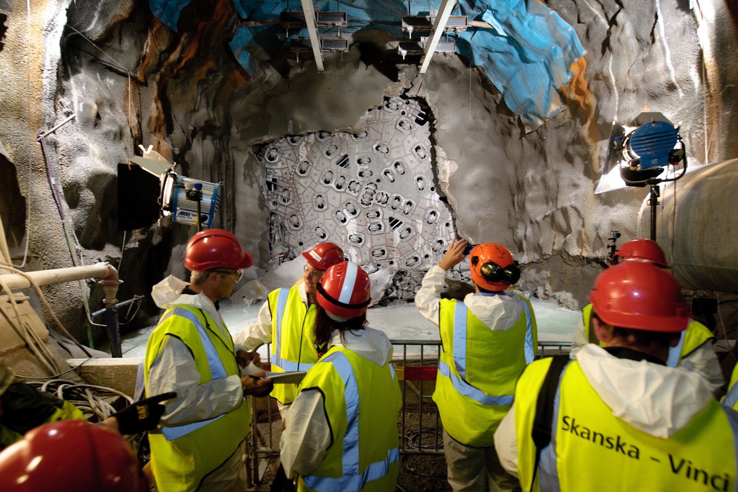 Hallandsås Byggnadsarbetare i skyddsutrustning inspekterar ett tunnelprojekt upplyst av starka lampor.