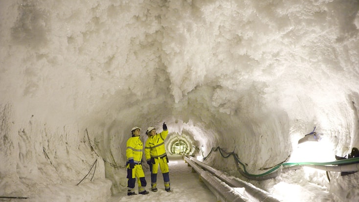 Hallandsås Två arbetare i säkerhetsutrustning undersöker iskalla formationer inne i en stor underjordisk tunnel.