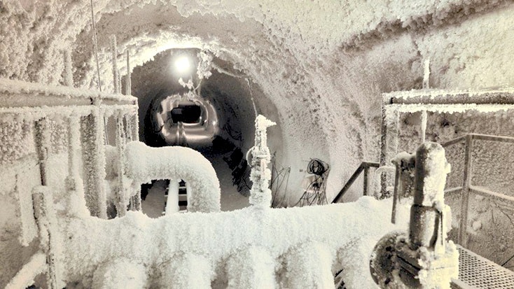 Hallandsås Fryst tunnelinteriör med frostiga rör och utrustning, upplyst av takbelysning.