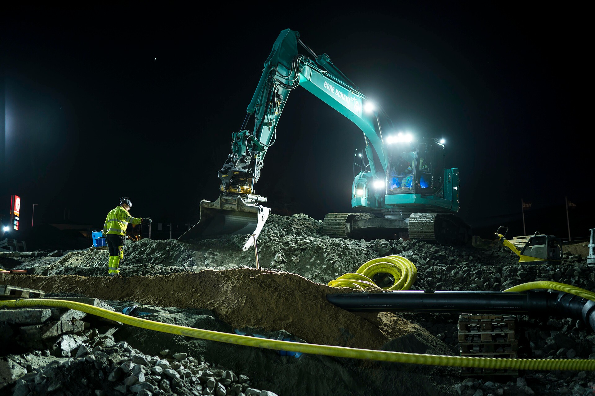 Arbetet pågick dygnet runt under påskhelgen. Byggarbetsplats på natten med en grävmaskin som gräver och en arbetare i säkerhetsutrustning som övervakar processen.