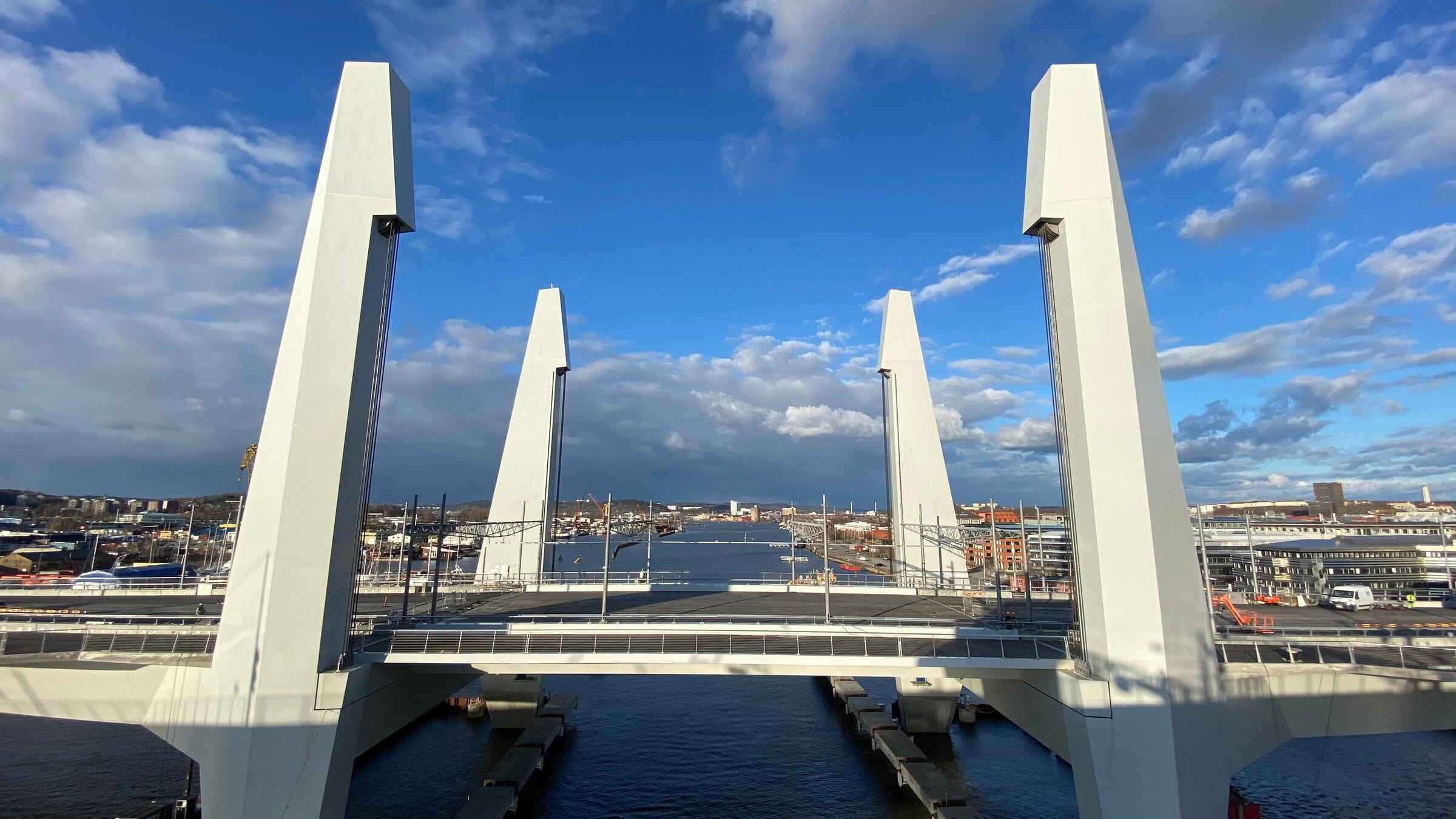 Modern snedkabelbro över en flod med en stadsbild och molnig blå himmel i bakgrunden.