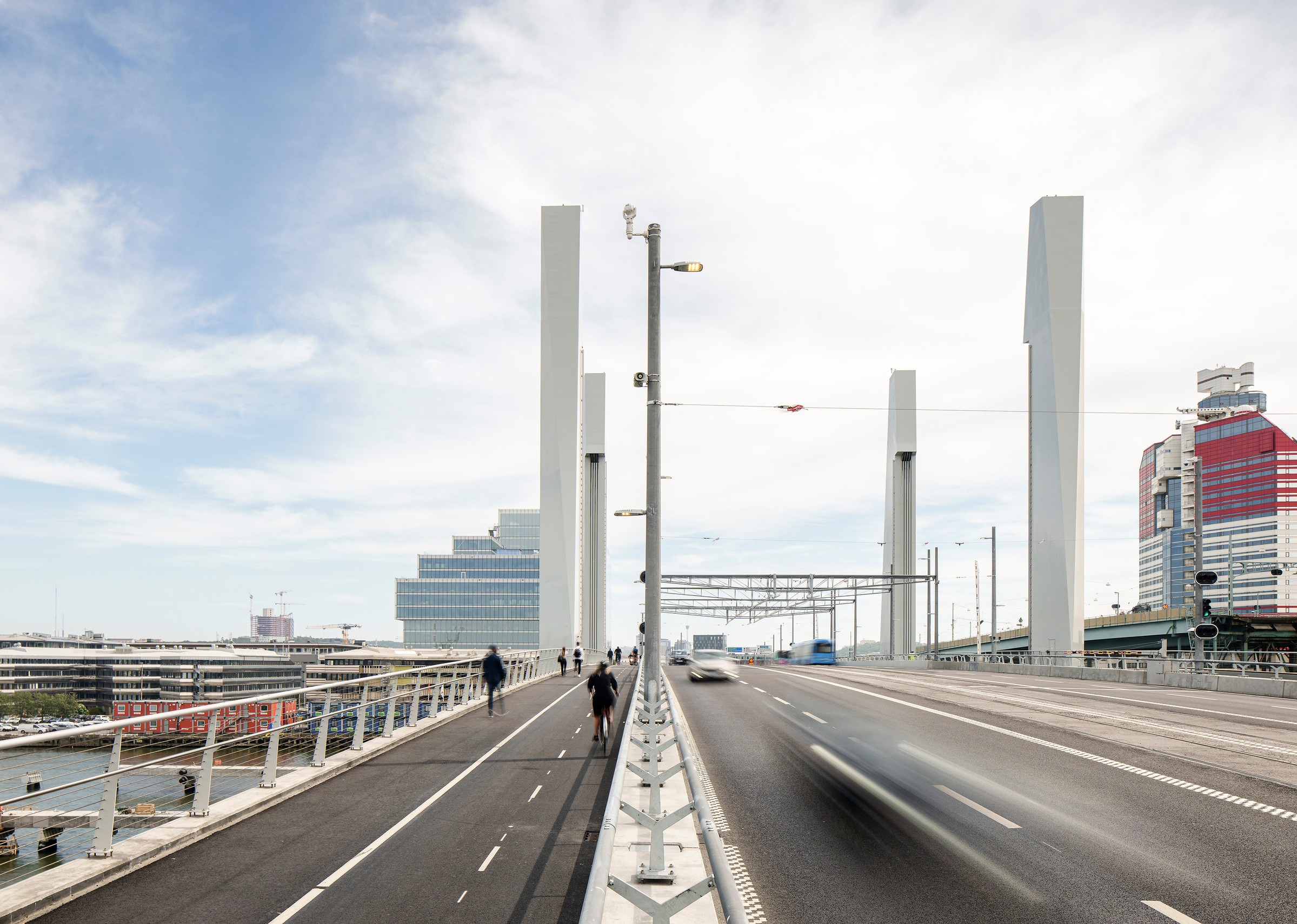 Under sommaren har ett intensivt arbete pågått för att koppla om spåren från den gamla Götaälvbron till Hisingsbron och färdigställa kollektivtrafikbron. Den 16 augusti 2021 rullade den första spårvagnen i linjetrafik över bron. Foto Felix Gerlach Modern bro med separata körfält för fordon och gångtrafikanter under en klar himmel i stadsmiljö.
