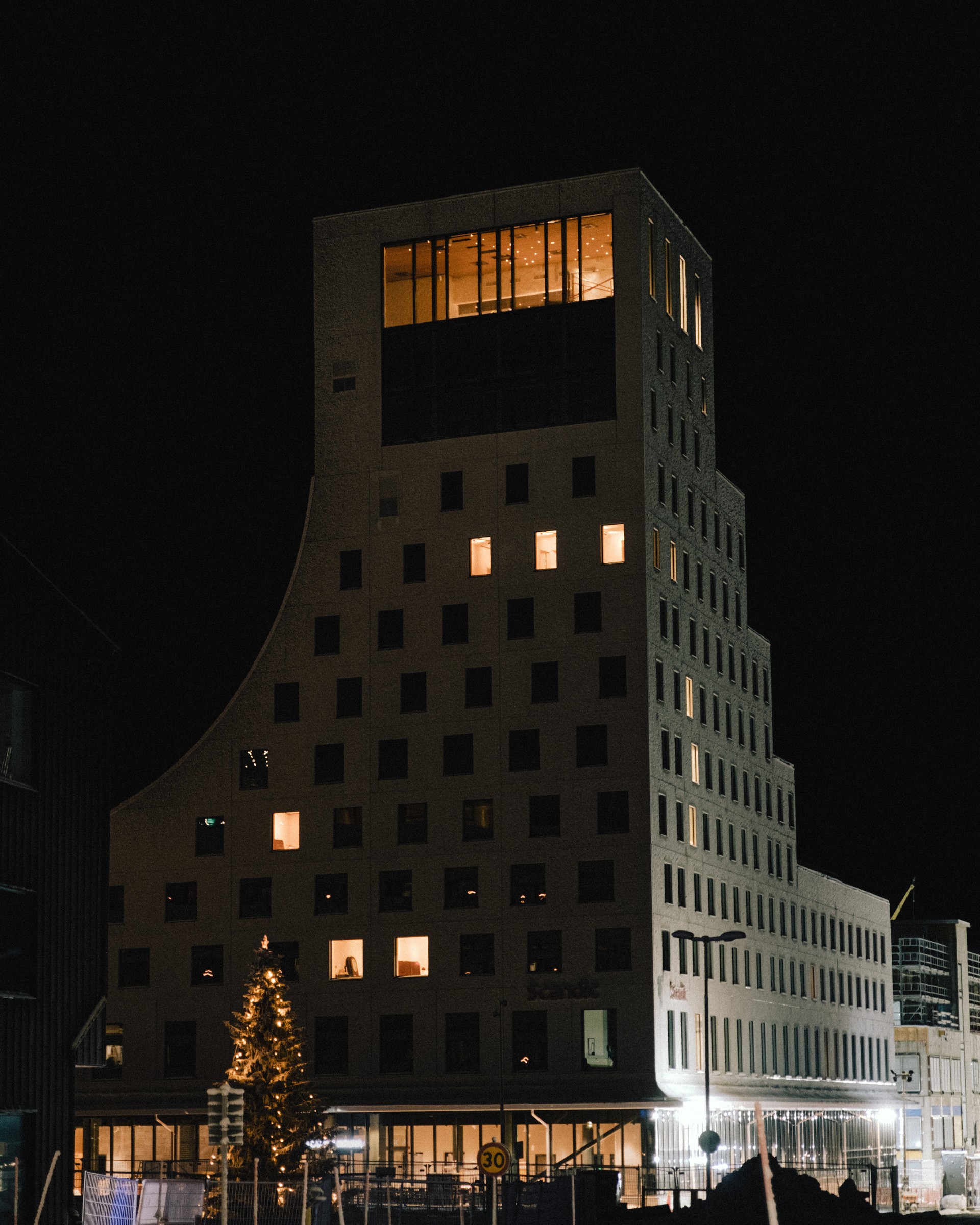 Modern fler våningsbyggnad upplyst på natten, med unik fönsterarrangemang och en böjd fasad.