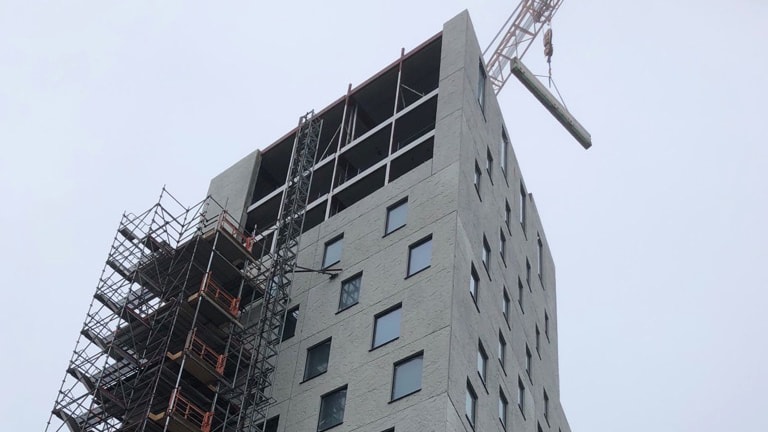 Höghus under konstruktion med byggnadsställningar och en kran som lyfter material.