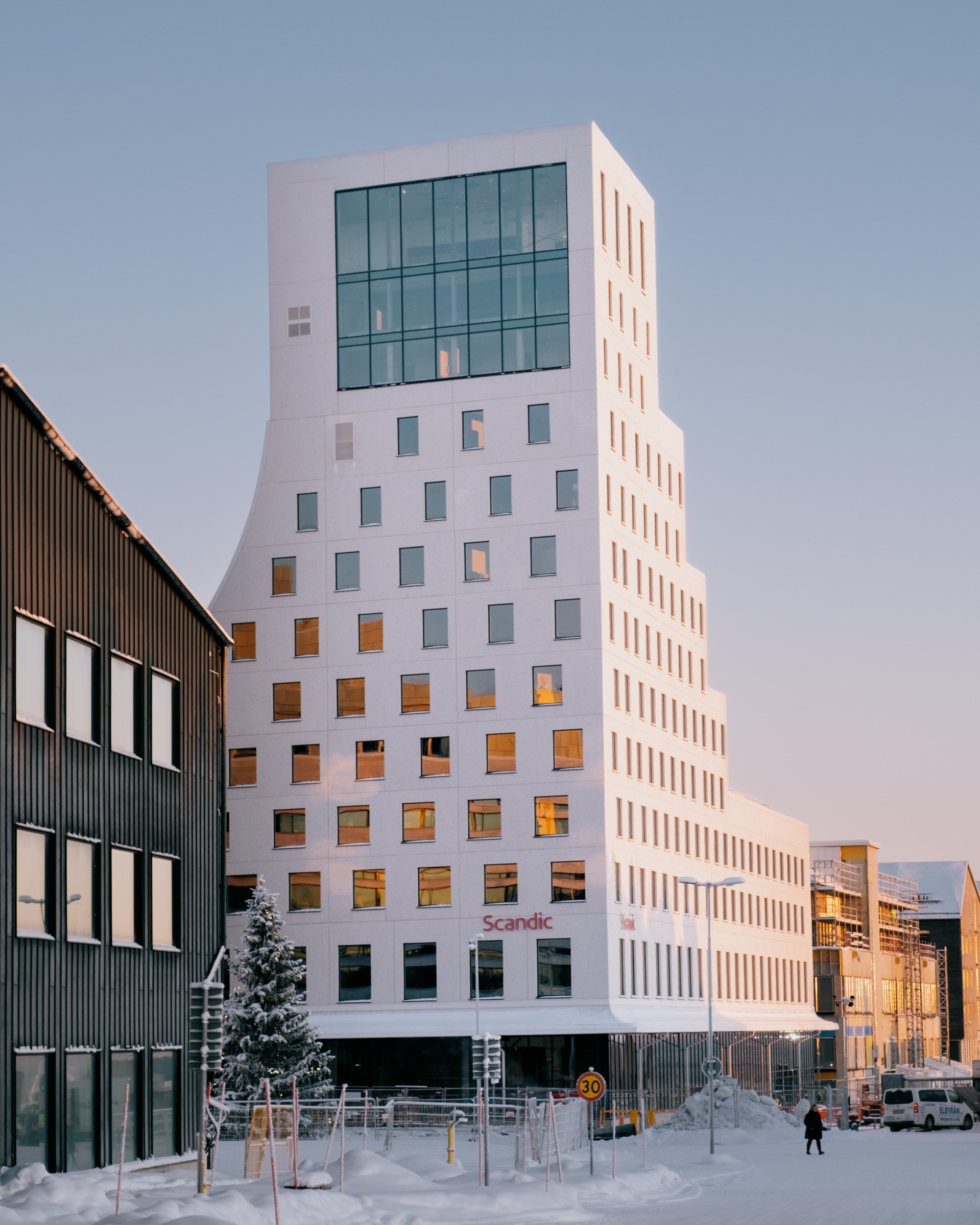 Modernt vitt höghushotell med unika fönstermönster, omgivet av snötäckt gata.