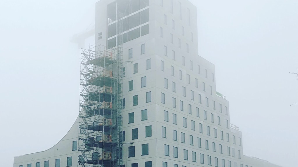 Dimma utsikt över en modern byggnad under konstruktion med byggnadsställningar på ena sidan.