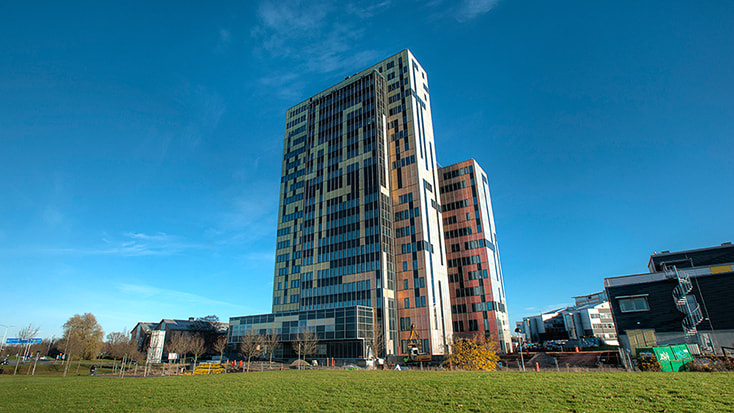 Modern byggnad i flera våningar med färgglad geometrisk fasad mot en klarblå himmel.