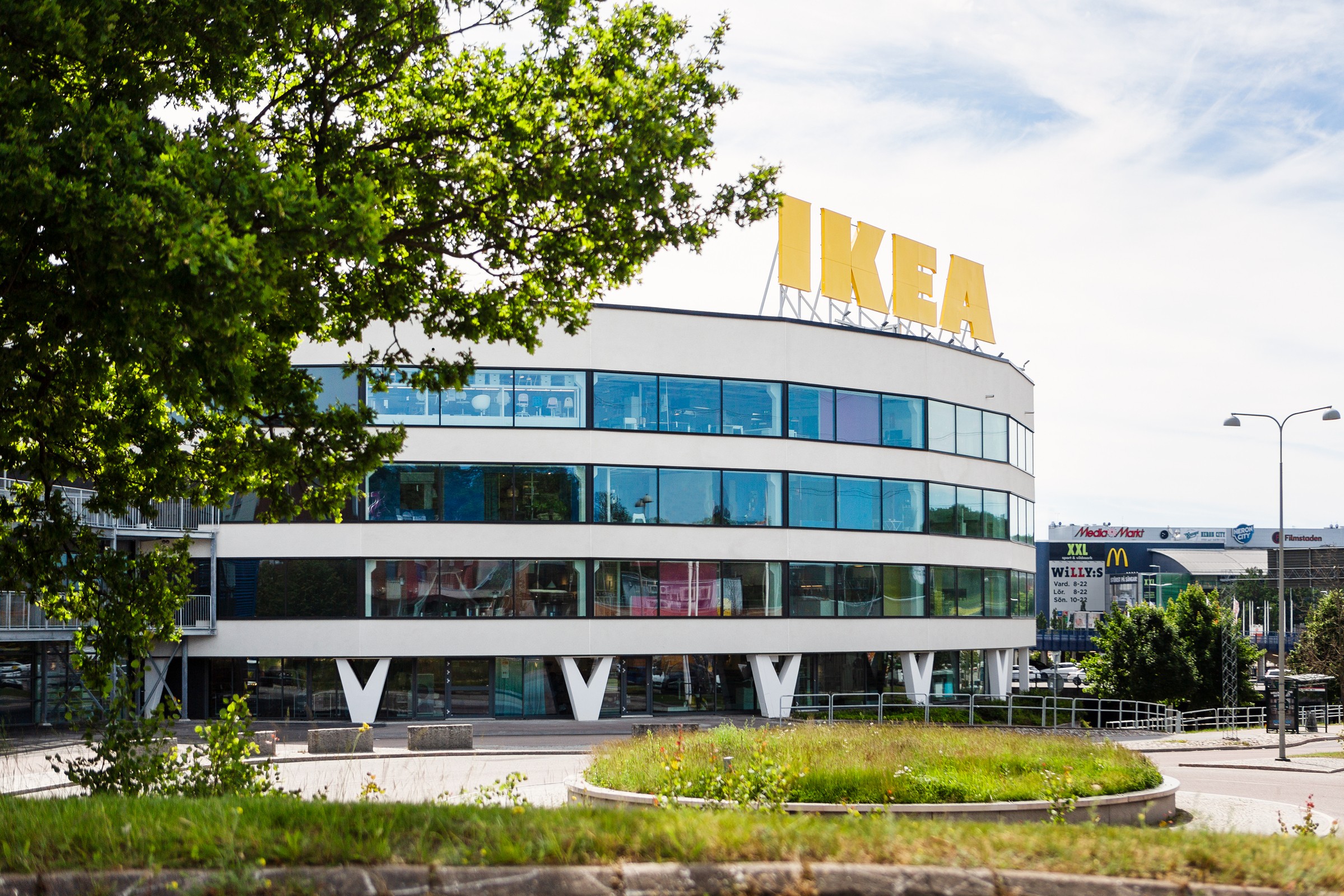 IKEA-butiks exteriör med modern arkitektur, omgiven av grönska under en klarblå himmel.