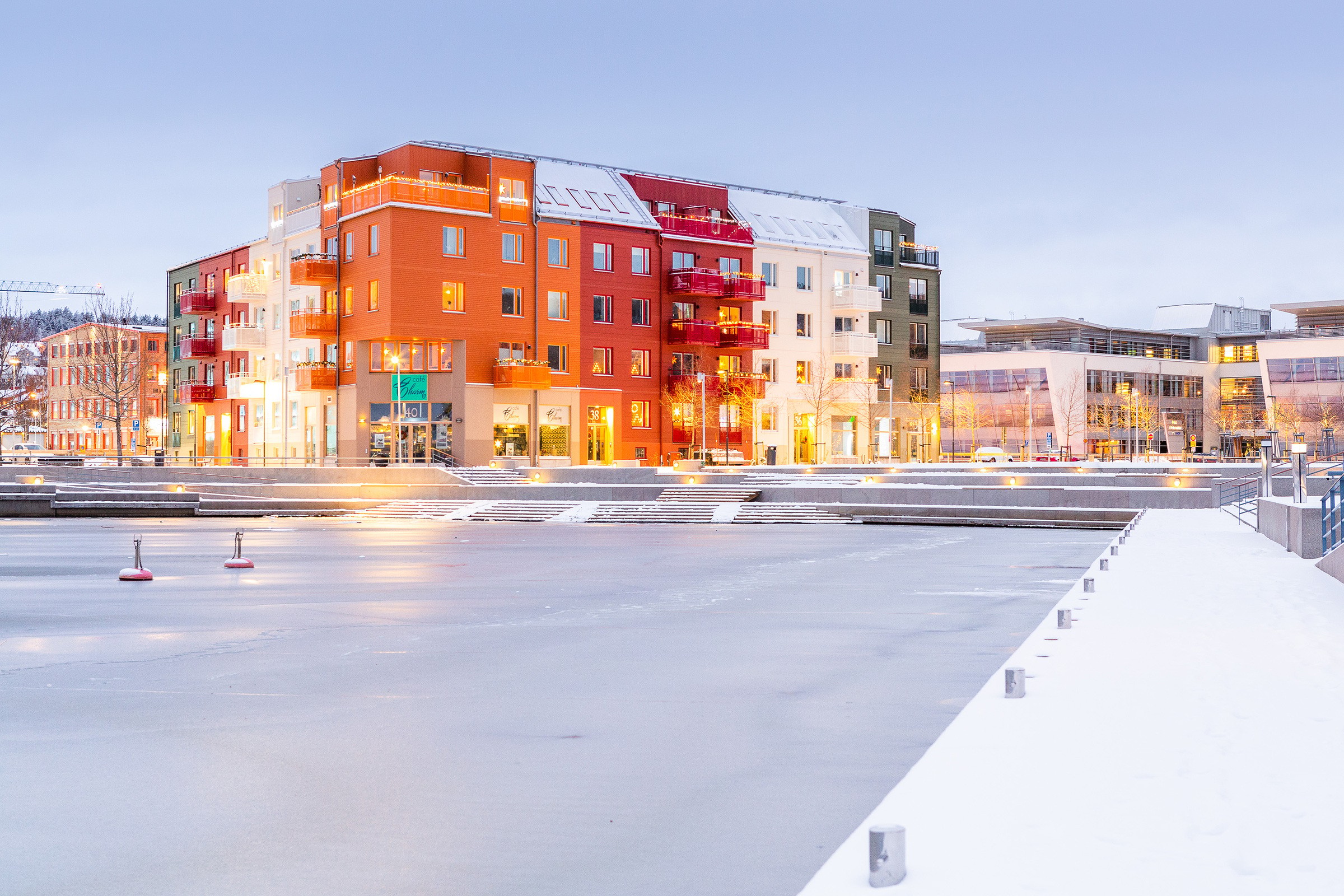 Färgglada moderna lägenheter vid en frusen strandlinje i en snöig stadsmiljö i skymningen.