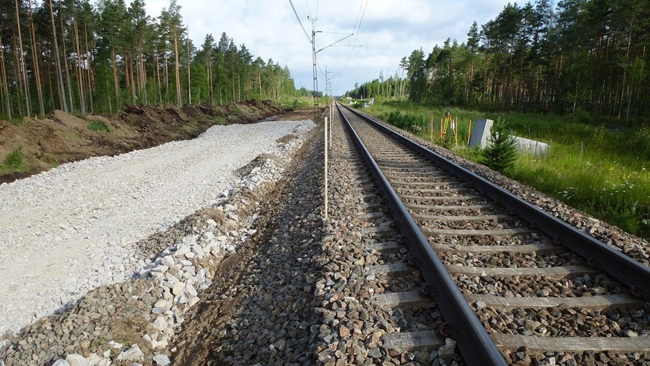 Stenkumla-Dunsjö är en av de första totalentreprenaderna på järnväg som Trafikverket har beställt. Järnvägsspår bredvid en grusstig i ett frodigt skogsområde under en delvis molnig himmel.