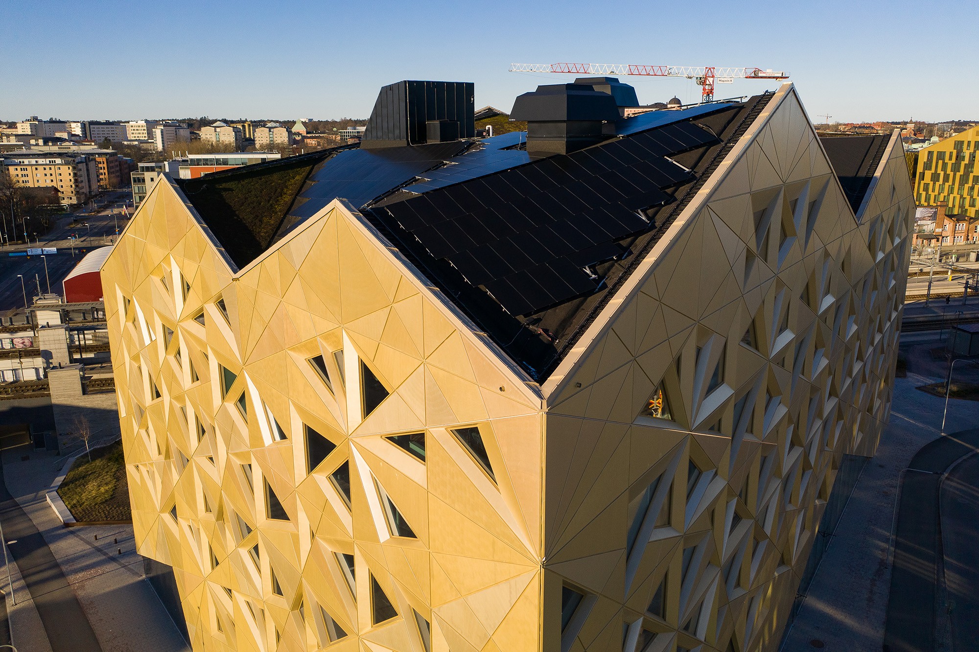 Modern geometrisk byggnad med solpaneler på taket i ett urbant landskap under klar himmel.