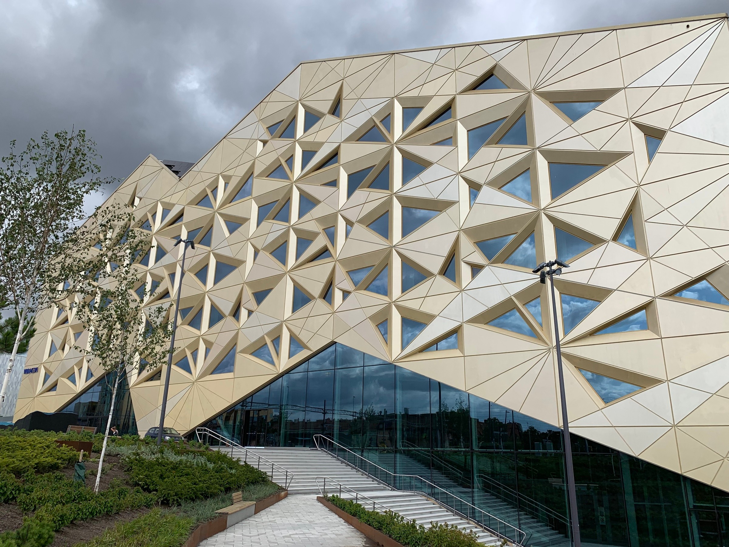Modern byggnad med geometrisk fasad, med triangulära fönster och en trappentré.