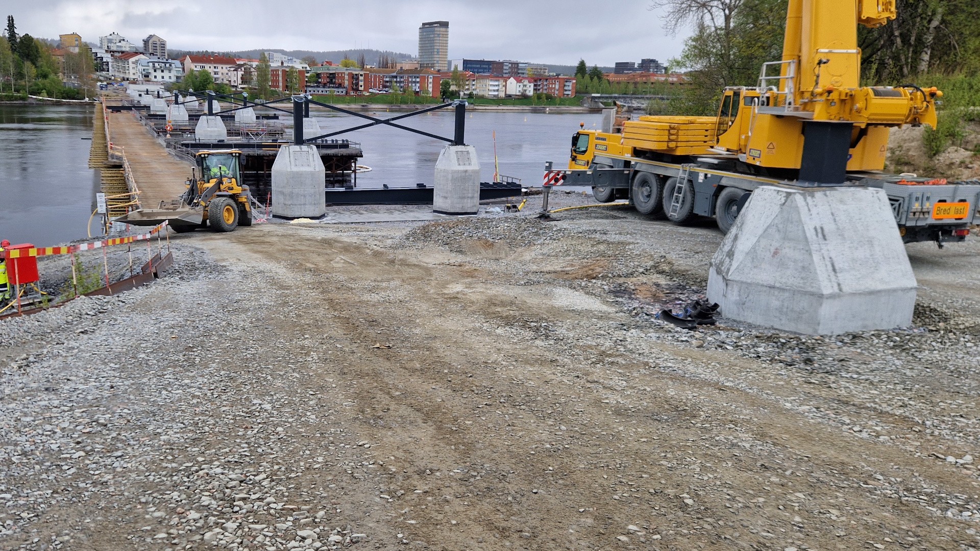 Byggarbetsplats vid Karlgårdsbron i Skellefteå med kran, grävmaskin och betongfundament i älven.