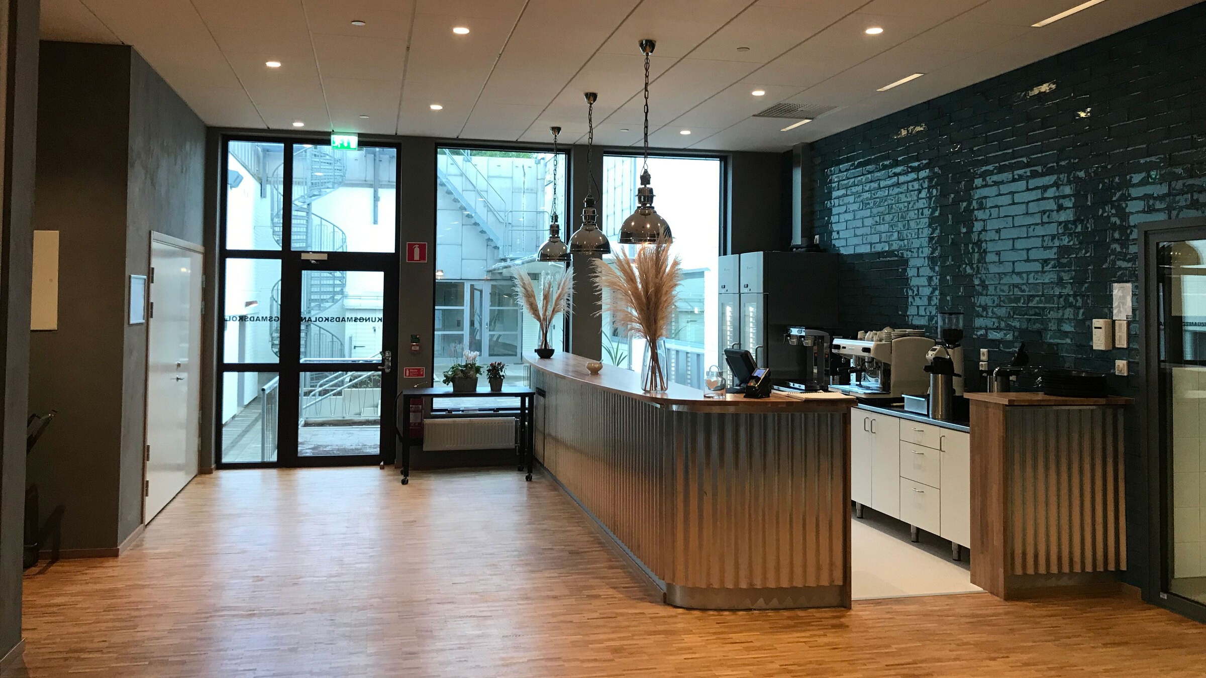 Modern kontorspausområde med en korrugerad metallbänk, hängande lampor och kaffestation.