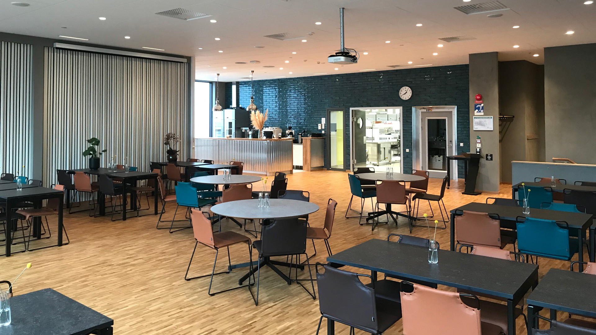 I matsalen serverar restaurangskolan sin mat. Modern matsal med varierande sittplatser, trägolv och utsikt över en elegant köksbänk.