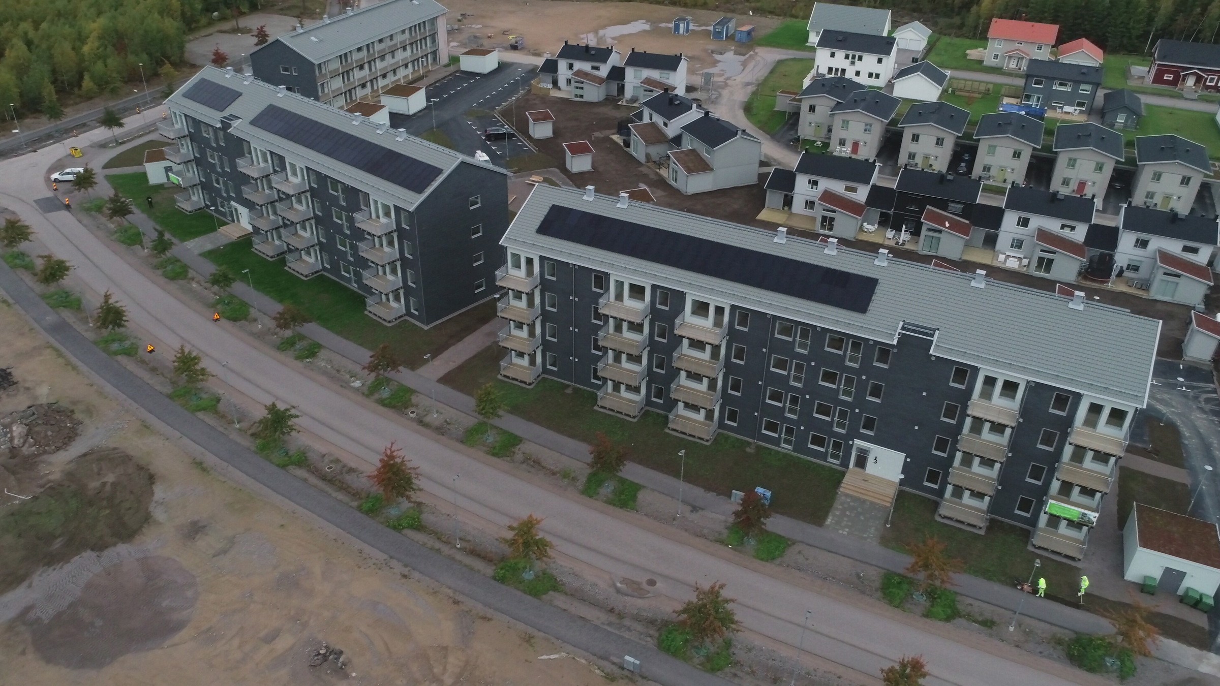 Flygvy av ett modernt bostadskomplex med flerfamiljshus och anlagda gångvägar.