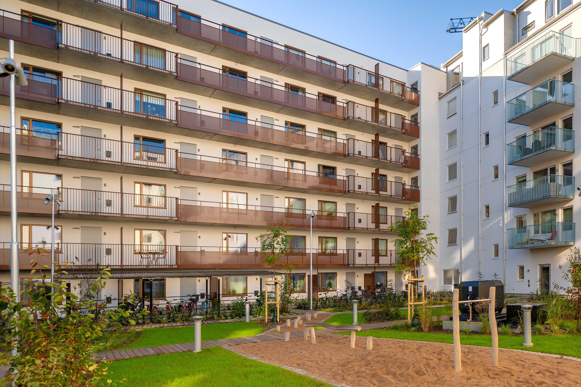 Grön innergård med plats för avkoppling, gemenskap och aktiviteter. Innergård med lekpark, gräsmatta och träd omringad av bostadshusens fasader.