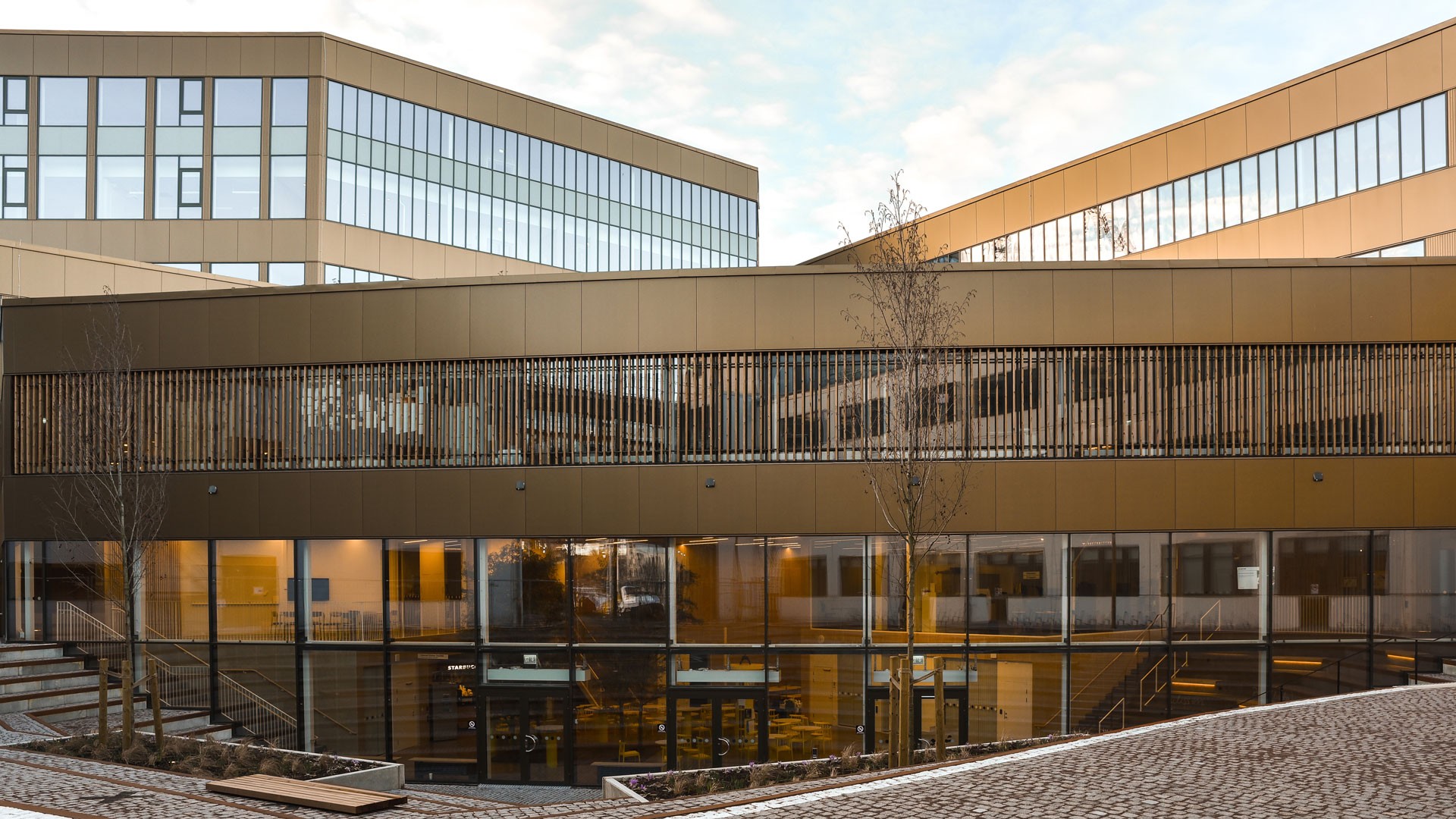 Modern kontorsbyggnad med stora fönster och elegant arkitektur, omgiven av en stenlagd gångväg.