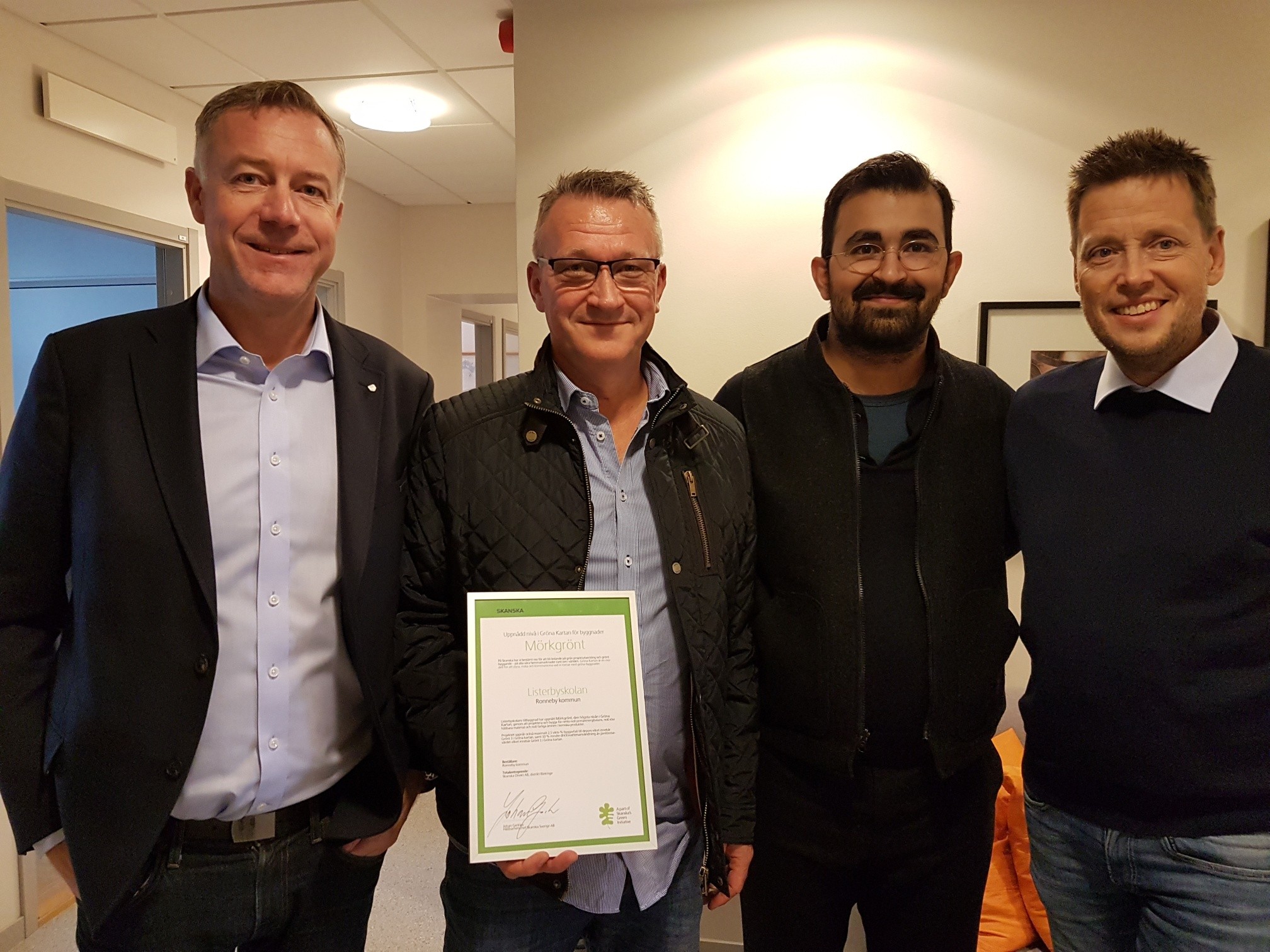 Fyra personer står inomhus och håller ett certifikat Fyra personer står inomhus och håller ett certifikat