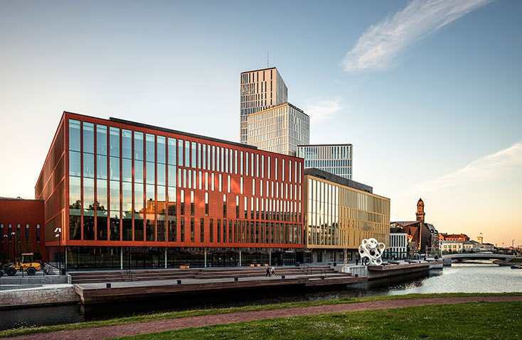 Malmö Live Modern byggnad vid vattnet med glasfasad bredvid kanal, med urban arkitekturdesign.