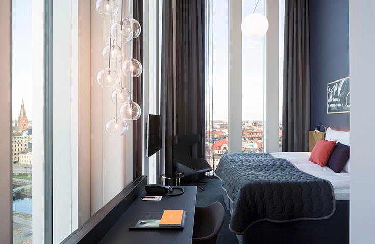 Malmö Live Modern hotellrum med stora fönster, utsikt över staden, mörka möbler och stilfull belysning.