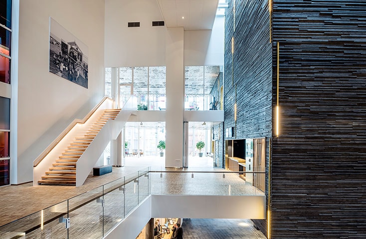 Malmö Live Modern interiör med trätrappa, glasräcken och strukturerad vägg i en rymlig lobby.