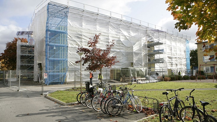 Brogården Byggnad under renovering med byggnadsställning, omgiven av cyklar och höstträd.