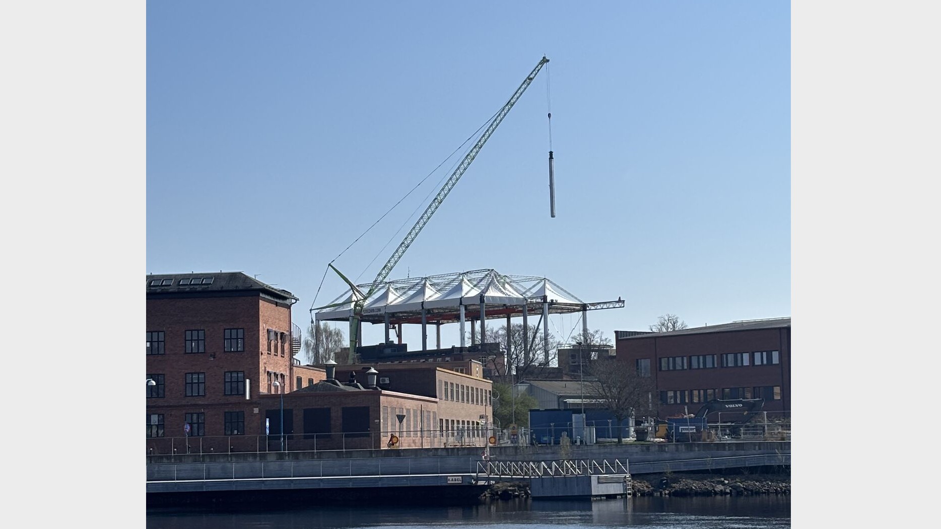Projektet är en del av Region Värmlands satsning på moderna vårdmiljöer. Vy över Klarälven mot Centralsjukhuset i Karlstad där ett nytt mottagningshus uppförs med synlig stålstomme och byggkran.