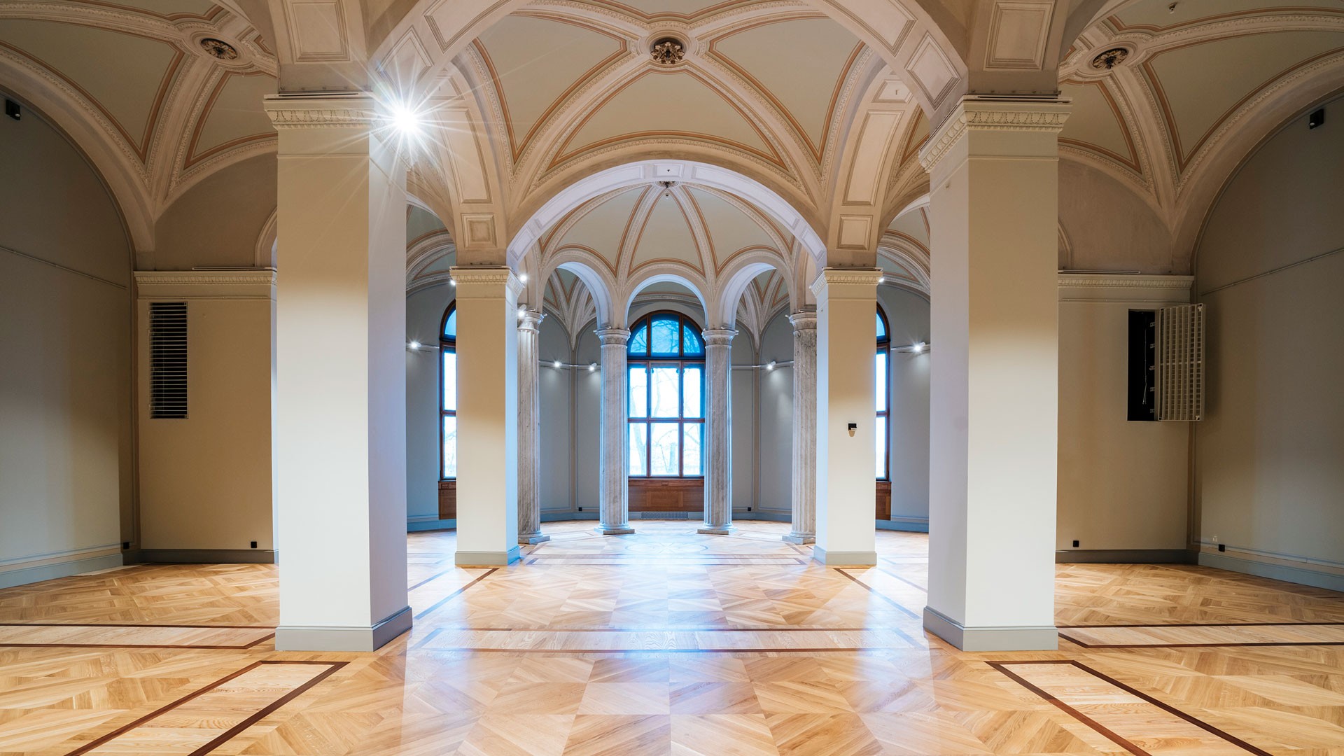 Elegant hall med valvformade tak, kolonner och stora fönster, med polerade trägolv.