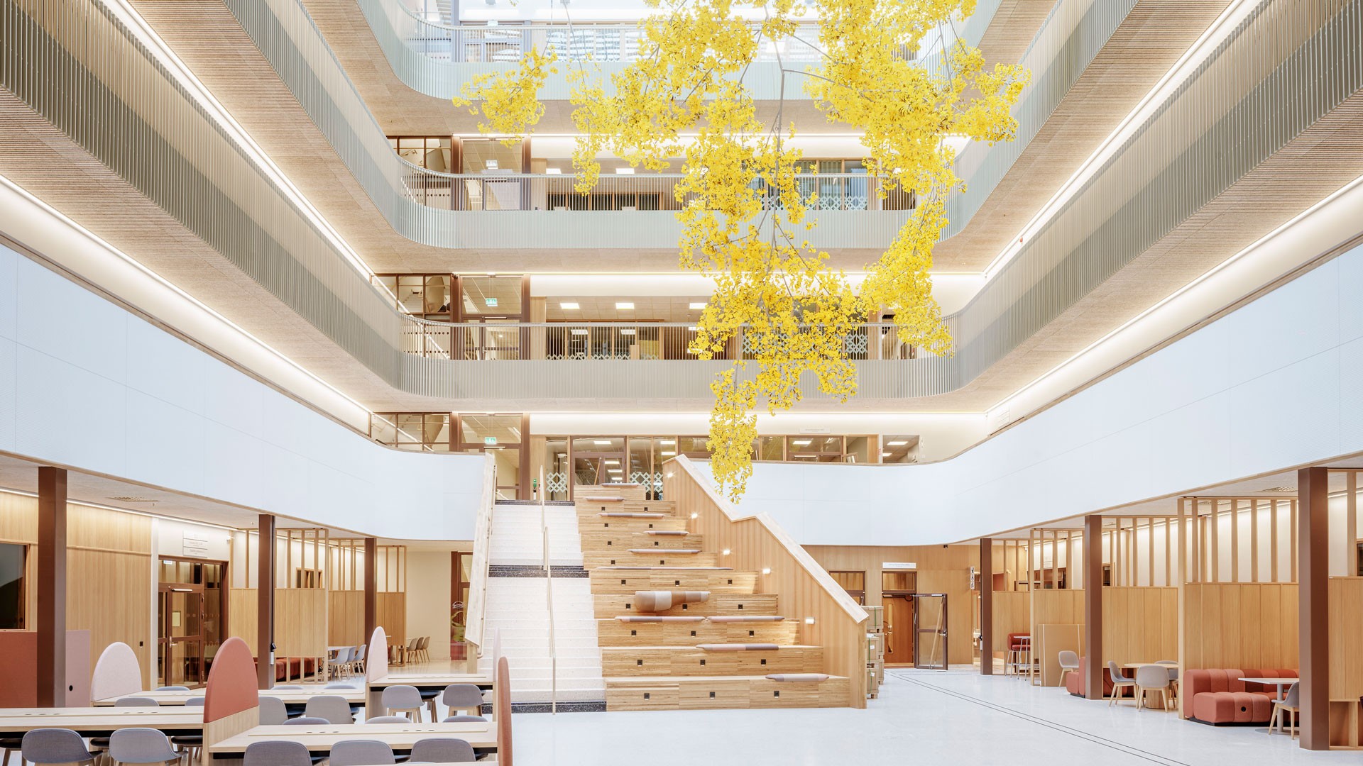Rymlig modern atrium med trädetaljer, sittplatser och en iögonfallande gul hängande installation.