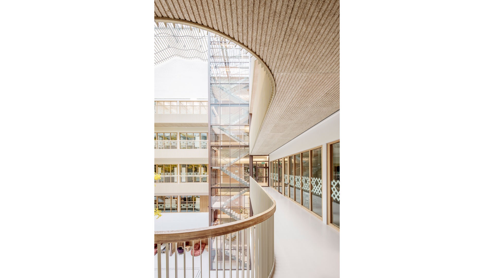Modern arkitektonisk interiör med böjd gångväg, glas-hiss och stora fönster.