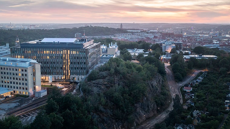 Flygvy av en modern byggnad på en klippig kulle, med utsikt över stadsbilden vid solnedgången.
