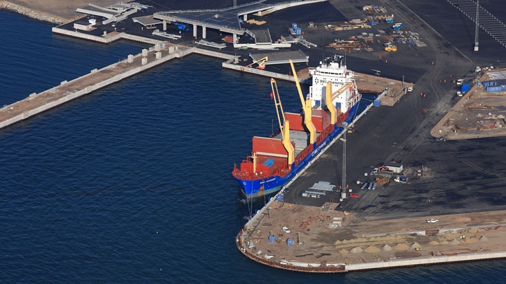 Norra Hamnen Flygvy av ett lastfartyg förtöjt vid en hamn, med kranar och containrar synliga på däck.