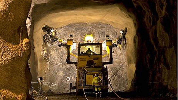Norra Länken 11 Underjordsgruvdrift med en tung borrmaskin och en arbetare i en svagt upplyst tunnel.